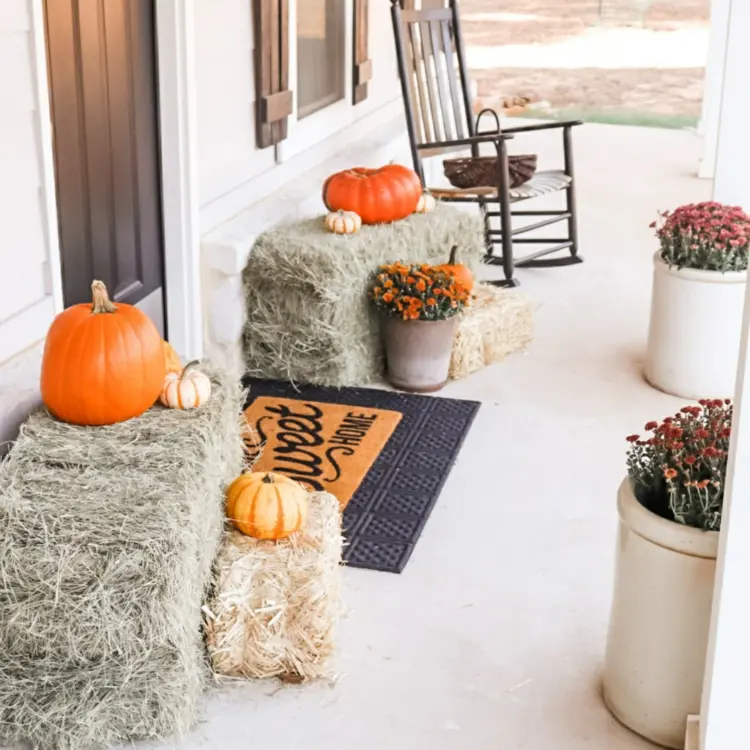 Haustür gestalten mit kleinen Ballen als Rahmen und Kübel mit Herbstblumen