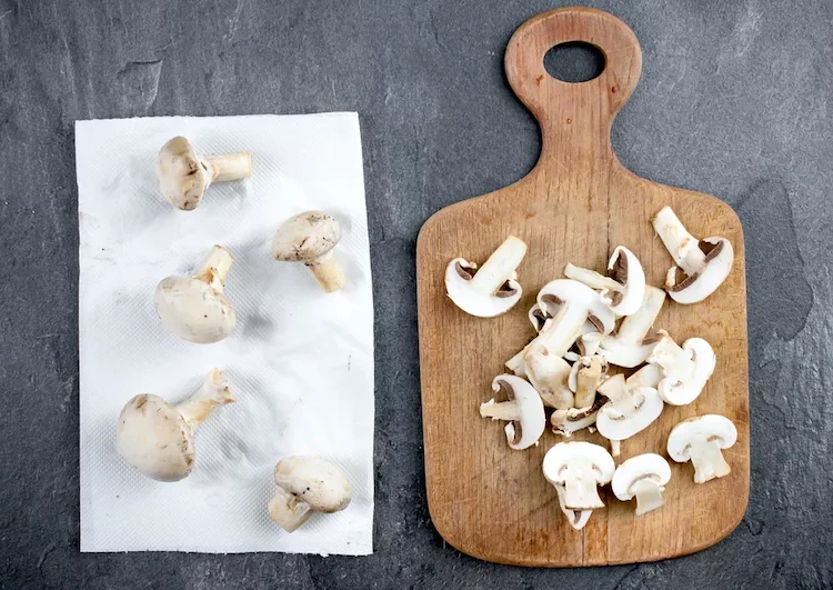ganze und in scheiben geschnittene champignons auf küchenpapier und auf küchenbrett trocknen lassen