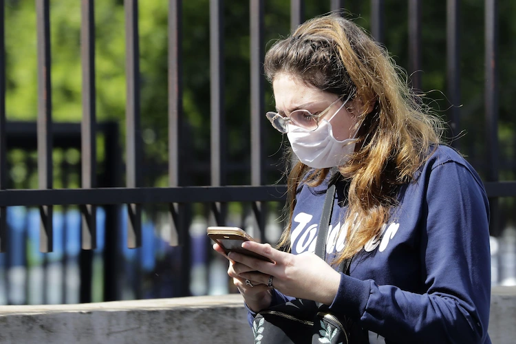 schutzmaske während der pandemie tragen und den bildschirm eines mobiltelefons mit fingern berühren