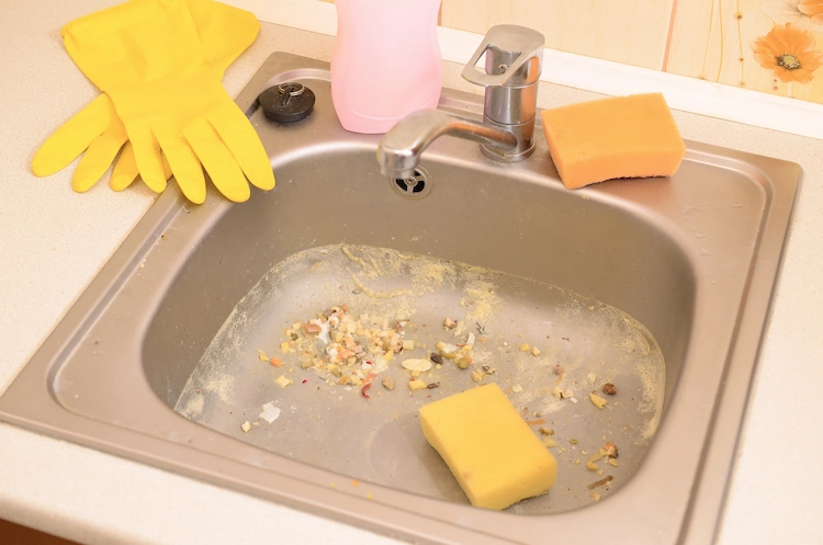 verstopfte küchenspüle durch essensreste mit gummihandschuhen und schwamm reinigen
