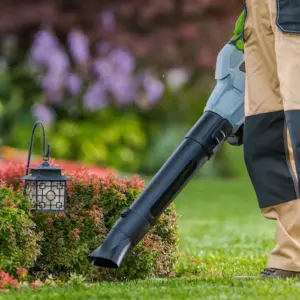 gärtner verwendet laubbläser auf ein blumenbeet auf rasenfläche