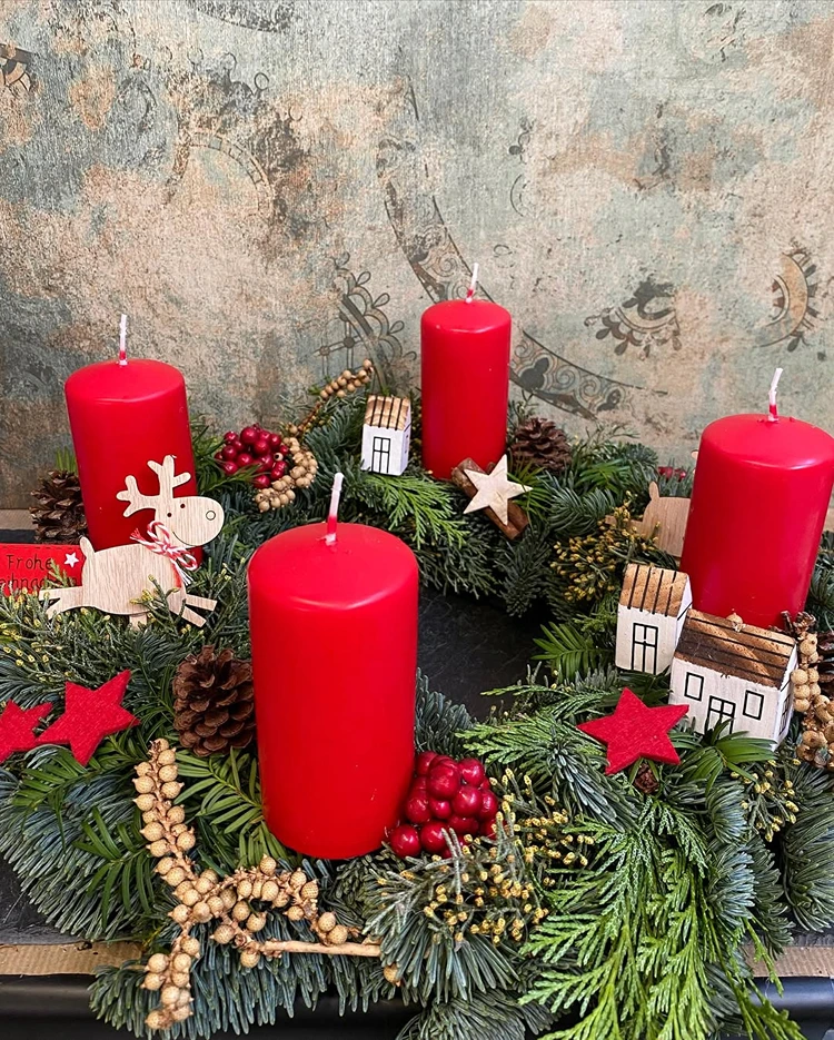 moderner adventskranz mit minihäusern und roten stumpenkerzen