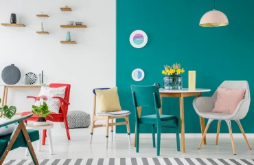 farbenfroh gestaltetes wohnzimmer mit blauer akzentwand und bunten stühlen