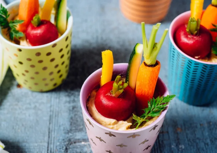 Tassen mit Hummus füllen und frischem Gemüse arrangieren