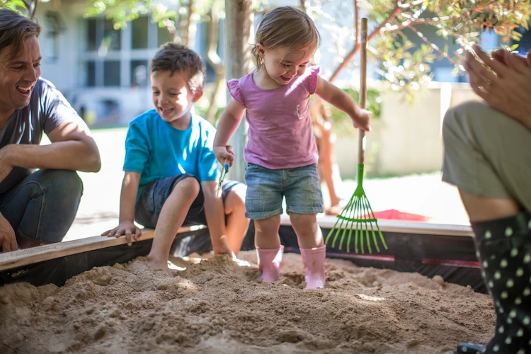 glückliche familie mit kindern beim spielen in einer sandkiste während des sommers