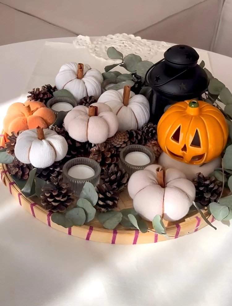 Arrangieren Sie mehrere Stoffkürbisse auf einem Dekoteller mit Tannenzapfen