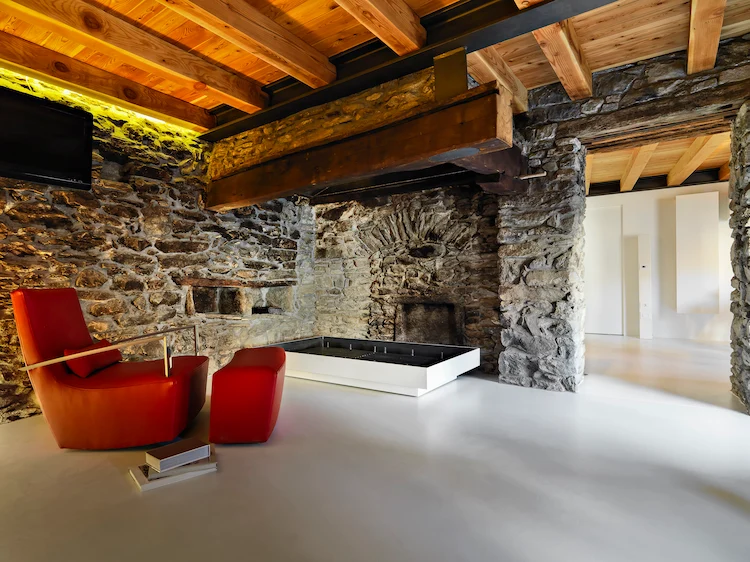 designer polstermöbel in rot passen zu rustikal gestaltetem wohnraum mit steinverkleidung und holzdecke