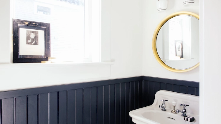 in marineblau und weiß gestaltetes badezimmer mit beadboard und goldenem spiegel