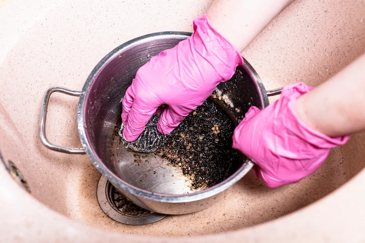 gummihandschuhe anziehen und mühsam einen eingebrannten topfboden reinigen in der küchenspüle durch kräftiges schrubben