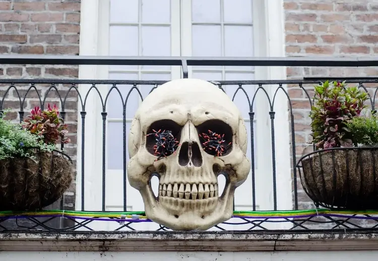 halloween deko für den balkon mit totenkopf, roter lichterkette und blumen am geländer