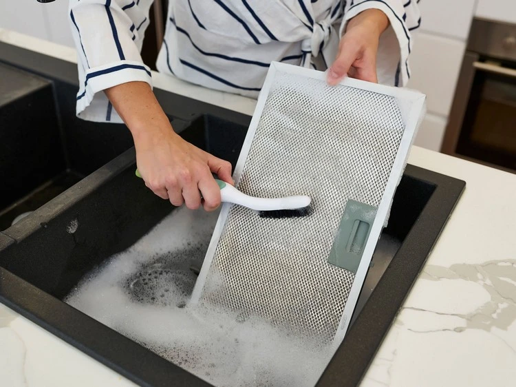 Klebrige Dunstabzugshaube reinigen - Fettige Filter ins Wasser legen und schrubben