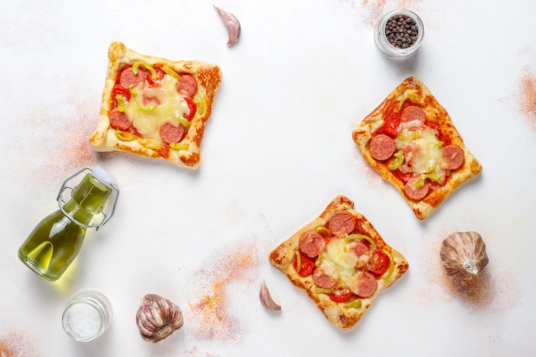 quadratische stücke pizza im blätterteig gebacken mit salami und käse darauf