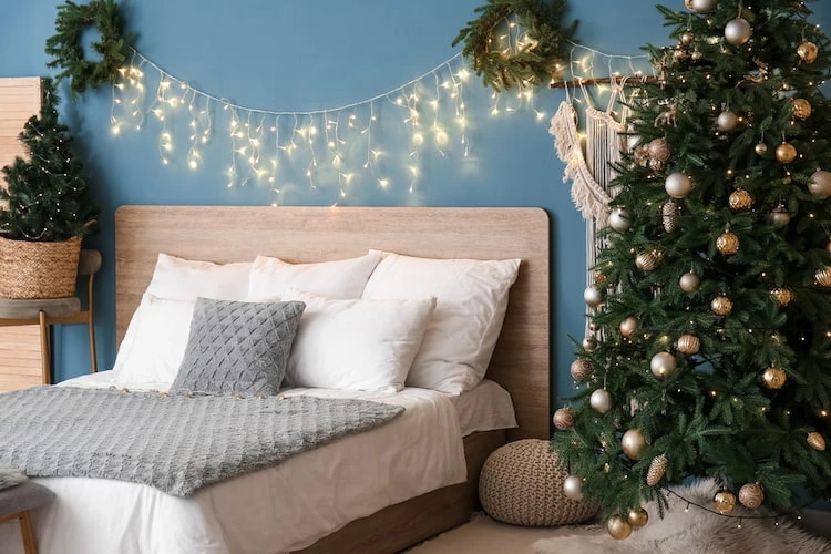 natürliche dekorationselemente wie tannenzweige und weihnachtsbaum mit lichterketten im schlafzimmer