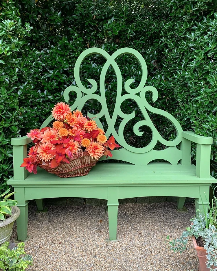 Dezente Deko auf einer grünen Vintage-Gartenbank mit orangen Dahlien im Korb