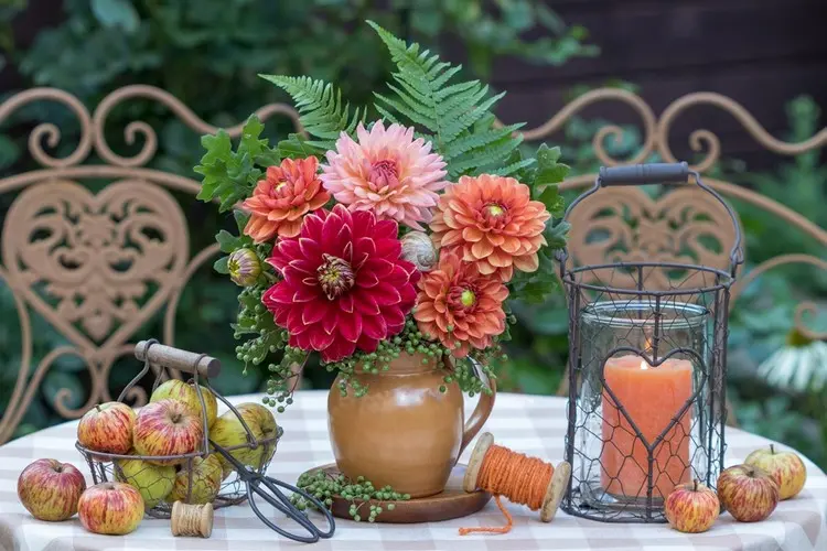 Rustikale Deko für den Gartentisch im Herbst mit orangen Blumen und Äpfeln der Saison