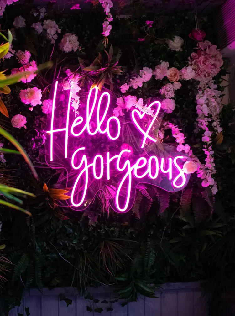 hello gorgeous neon schriftzug auf blühender pflanzenwand