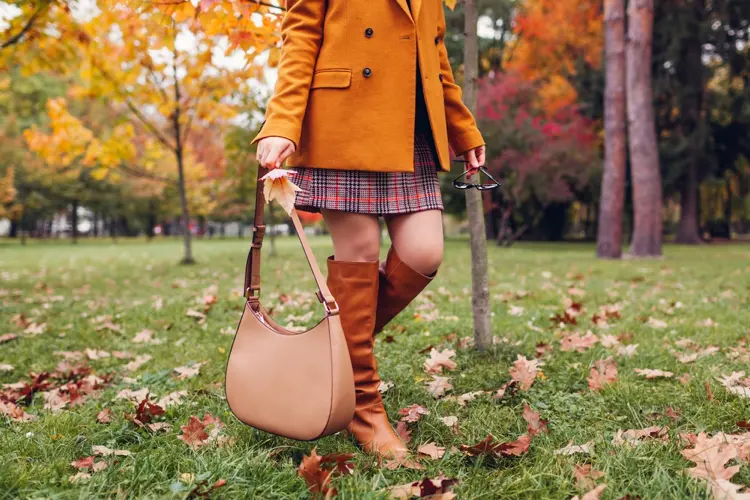 kniehohe braune stiefel mit kariertem kleid und orangenfarbenem mantel im herbst