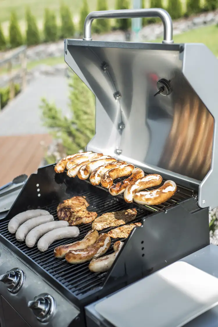 nahaufnahme eines gasgrills mit würstchen und fleisch für ein festmahl