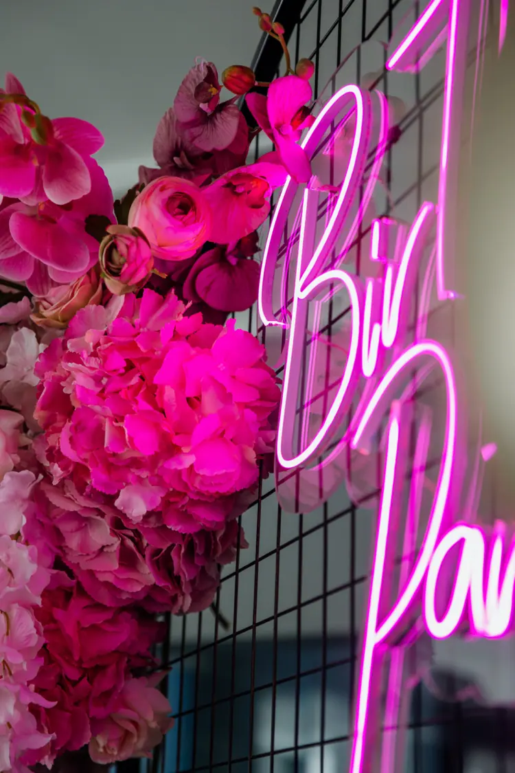 pinker neon schriftzug auf metallgitter mit blüten