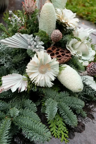 Weißer Grabschmuck mit Trockenblumen und Papierdeko auf immergrünen Zweigen