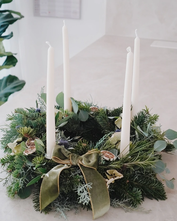 adventskranz mit weißen stabkerzen und feinem grün