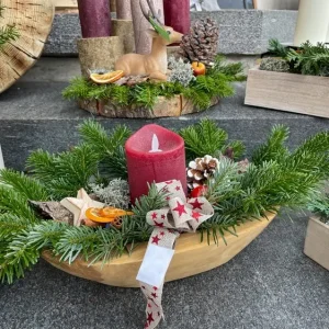 Holzschale mit Tannengrün, roter Kerze und weihnachtlichen Dekorationen