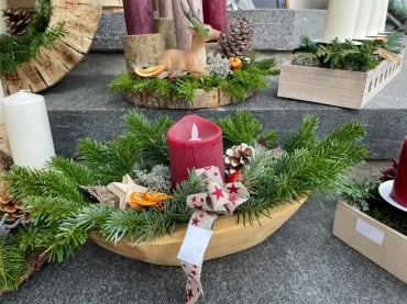 Holzschale mit Tannengrün, roter Kerze und weihnachtlichen Dekorationen