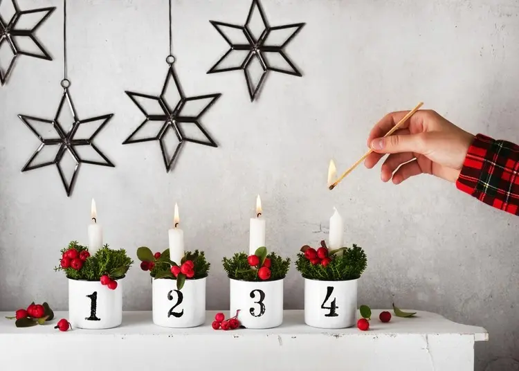 Moderne Alternative zum Adventskranz in Weiß mit Metallbechern, grünen Zweigen, Beeren und Tafelkerzen