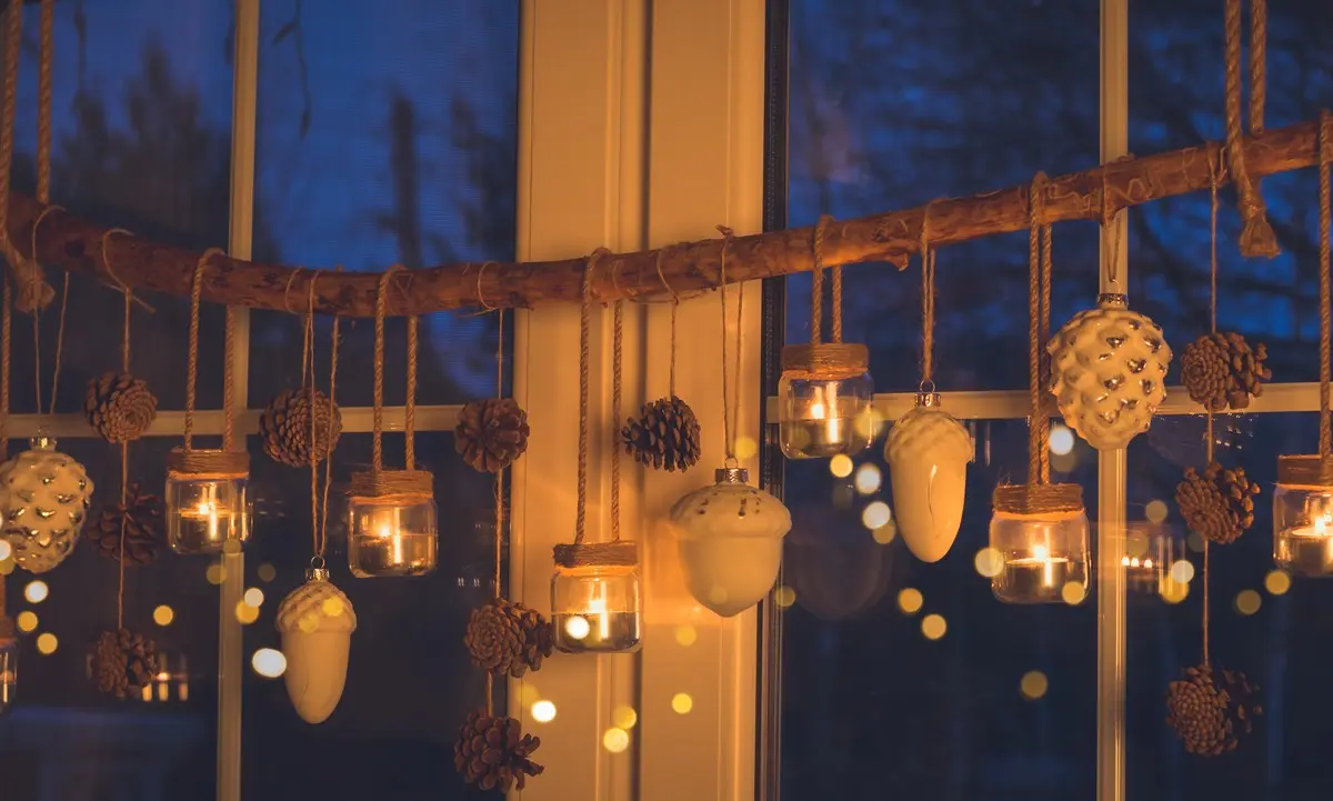 Hängende Fensterdeko für den Winter selber machen an einem Ast mit Windlichtern und Zapfen