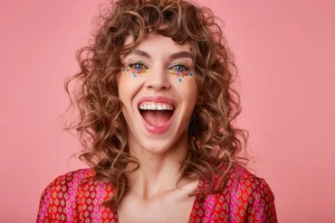 frau mit lockigem haar mit buntem konfetti make up lachend