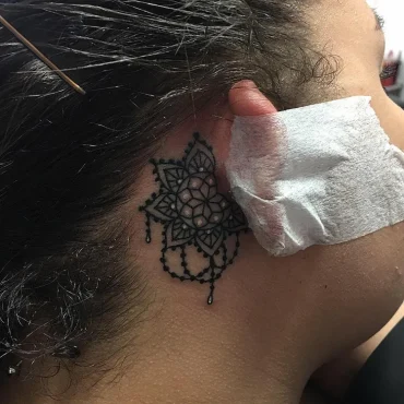 schönes mandala tatoo hinter dem ohr einer frau mit schwarzen haaren