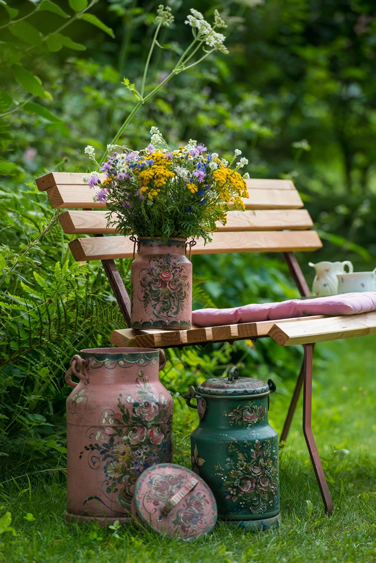 blumenstrauß in milchkanne bemalt auf gartenbank