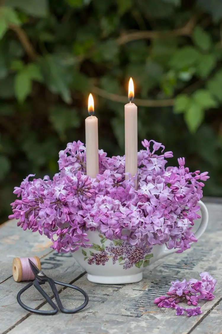 Flieder-Gesteck in einer Porzellantasse mit Kerzen für romantisches Licht am Abend