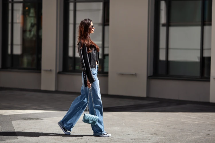 frau mit schlagjeans, schwarzer lederjacke und turnschuhen