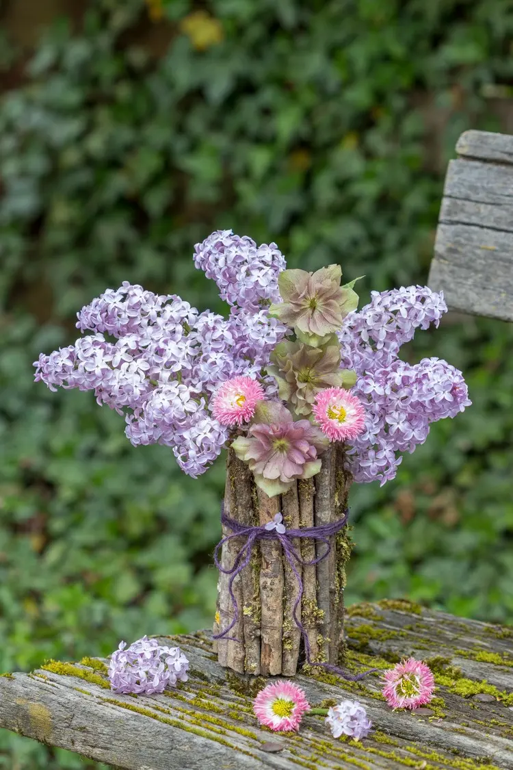 Natürliche Vase aus Stöckchen, mit Schnur umwickelt und Helleborus, Flieder und Gänseblumen