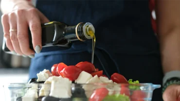 olivenöl über griechischen salat gießen für die mediterrane ernährung