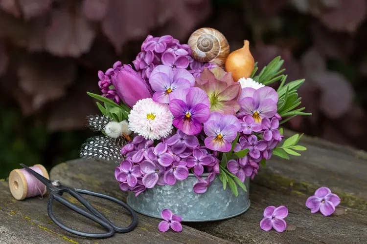 Tischdeko für den Garten mit Flieder, Hornveilchen, Gänseblümche und Schneckenhaus im Zinkgefäß