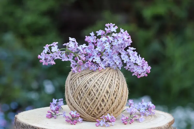 Tischdeko für den Garten mit Flieder in einem Garnknäuel statt Vase