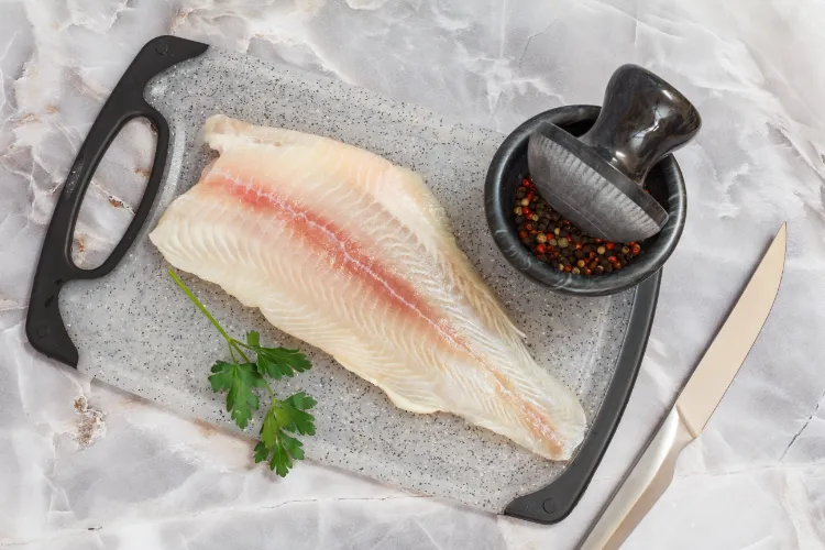 filet von rohen pangasius fisch mit petersilie blätter und gewürze auf einem schneidebrett