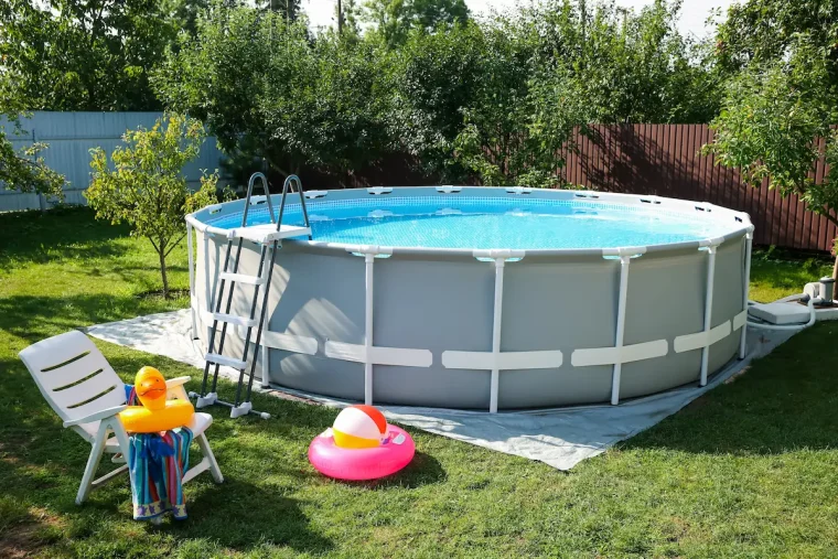 pool mit leiter und bodenschutzfolie auf grünem rasen, umgeben von gartenmöbeln und spielzeug