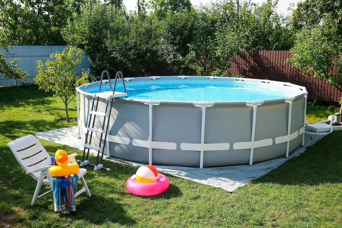pool mit leiter und bodenschutzfolie auf grünem rasen, umgeben von gartenmöbeln und spielzeug