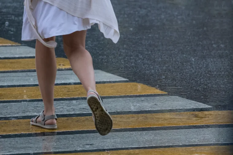 frau überquert bei regen die straße in offenen textilsandalen