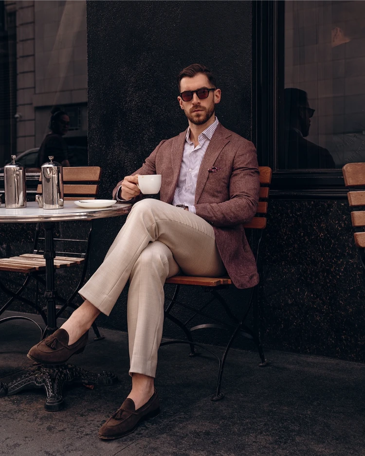 stilvoller mann mit leinenblazer, hemd, beiger hose und mokassins beim kaffeetrinken