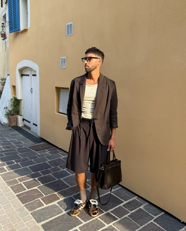 stilvoller mann mit schwarzem leinenblazer, schwarzen shorts und adidas schuhen