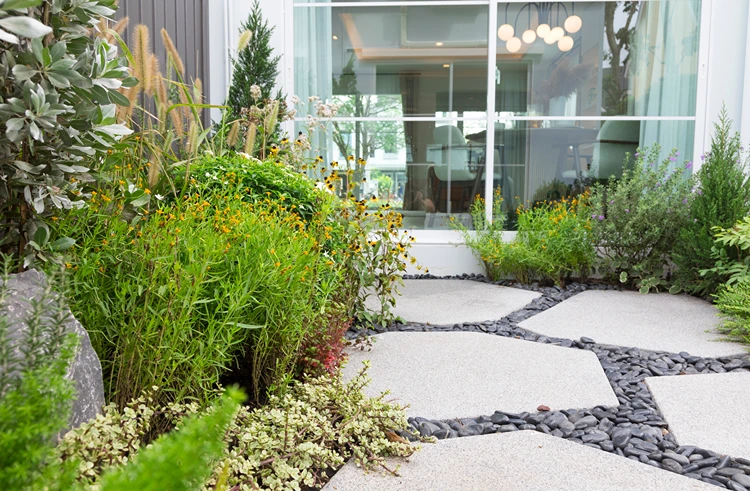 gestaltungsbeispiel für trittplatten auf schwarzem zierkies zwischen stauden im naturnahen garten