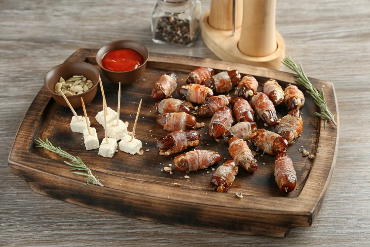 hölzerner tabletterträger mit mit speck umhüllten daten auf tisch