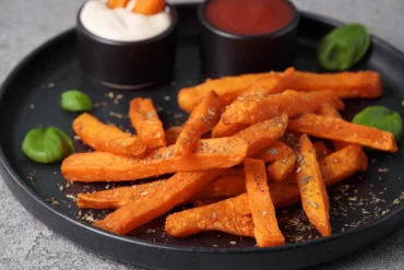 süßkartoffelsticks auf einem schwarzen teller, garniert mit mayonnaise und ketchup sauce