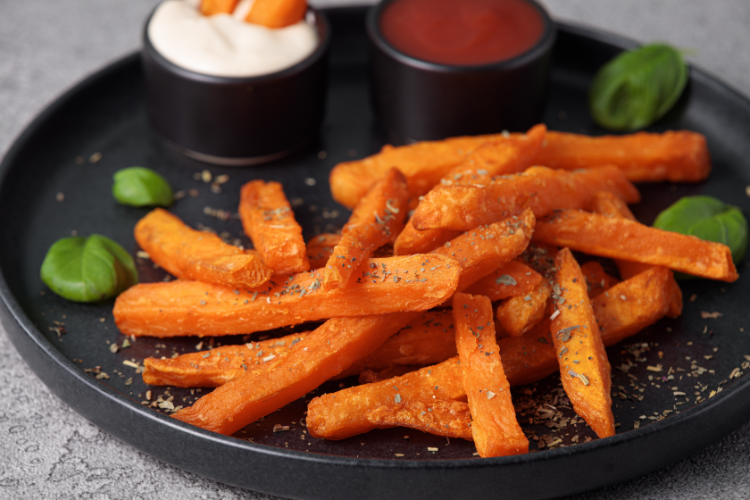 süßkartoffelsticks auf einem schwarzen teller, garniert mit mayonnaise und ketchup sauce