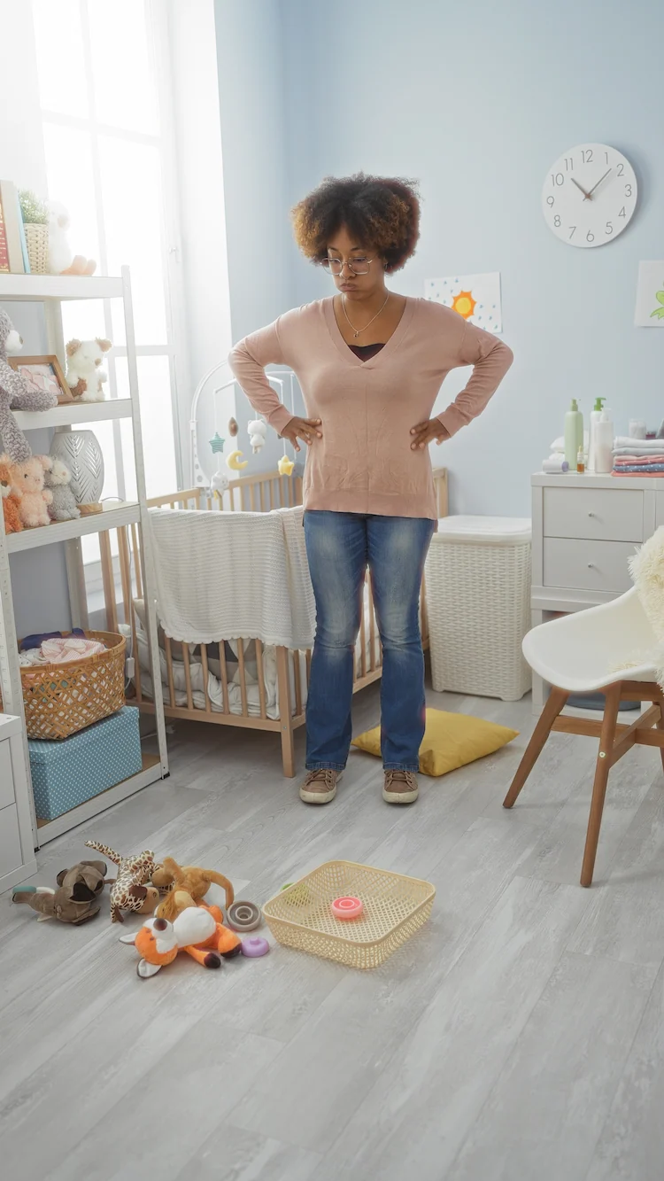 mutter blickt auf verstreutes spielzeug im babyzimmer – typisches chaos im alltag
