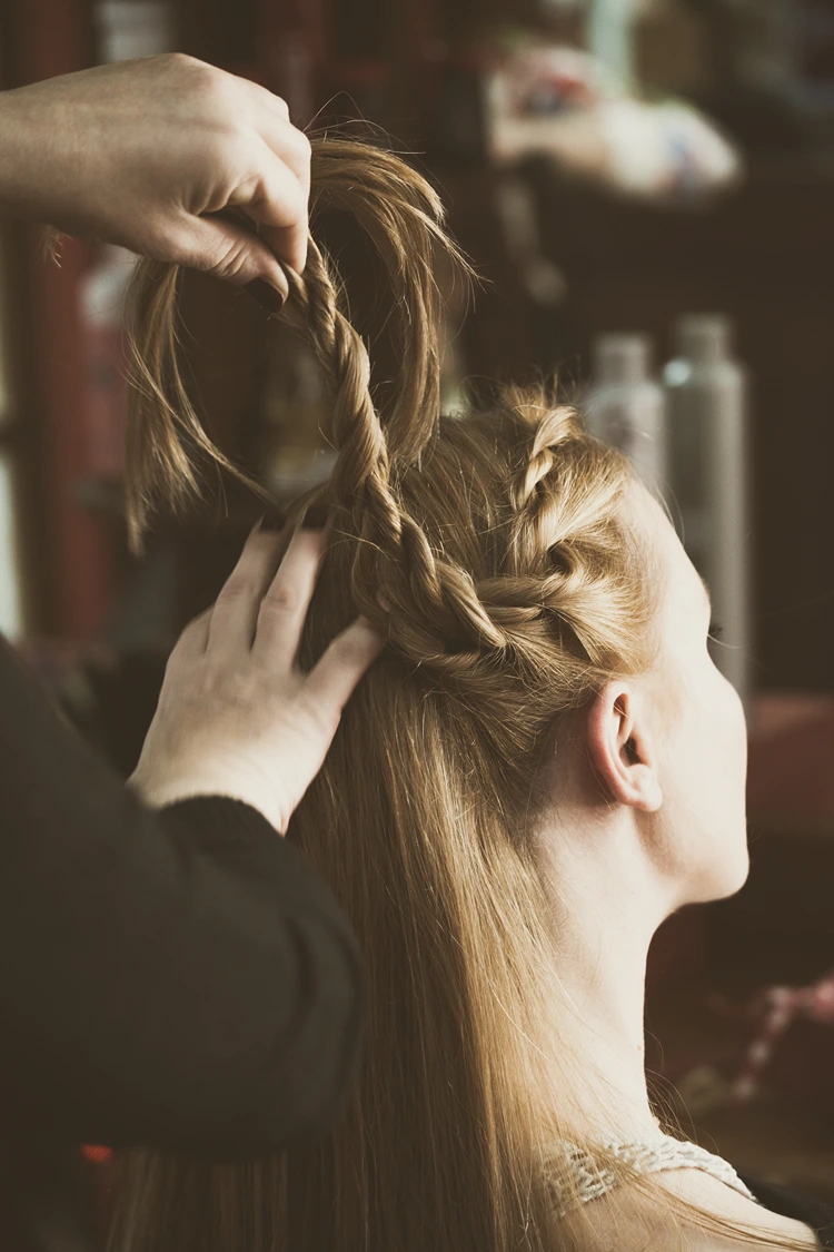 stylistin dreht strähnen seitlich ein, um eine voluminöse kordelzopf frisur fürs oktoberfest zu formen.